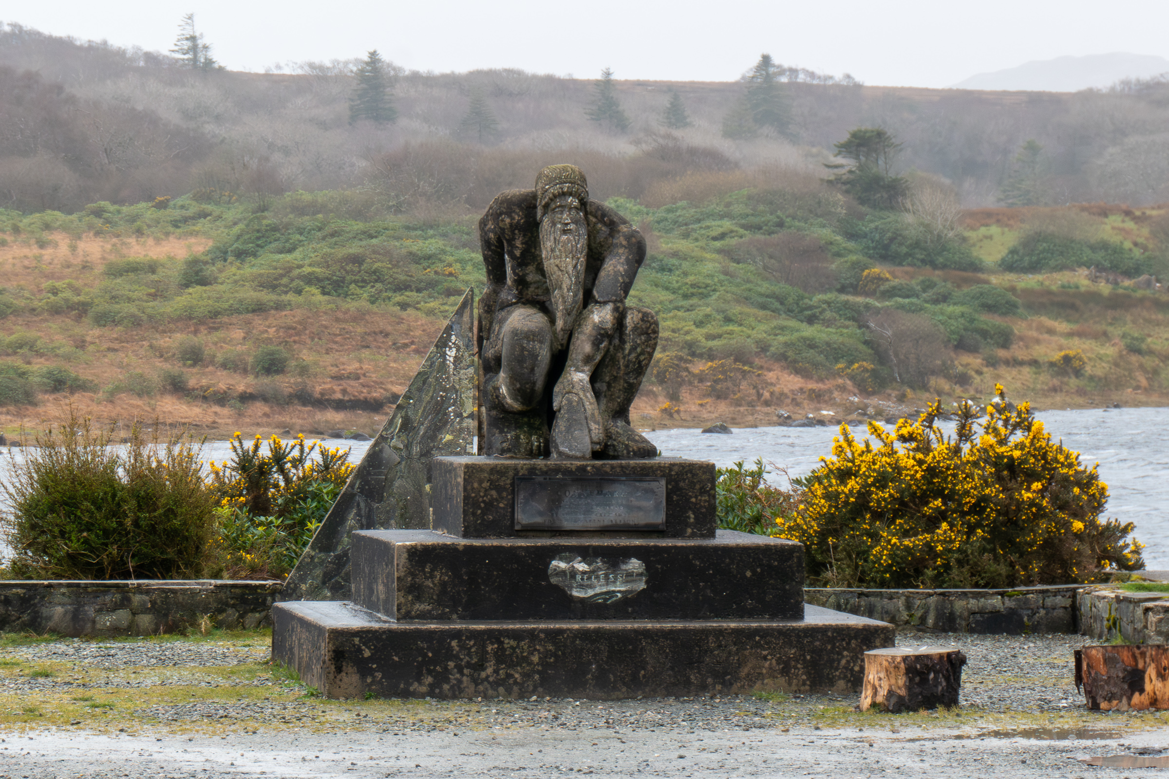 Photo of 'Connemara Giant' a concrete statute on the side of the road. There is a small lake behind the statue.