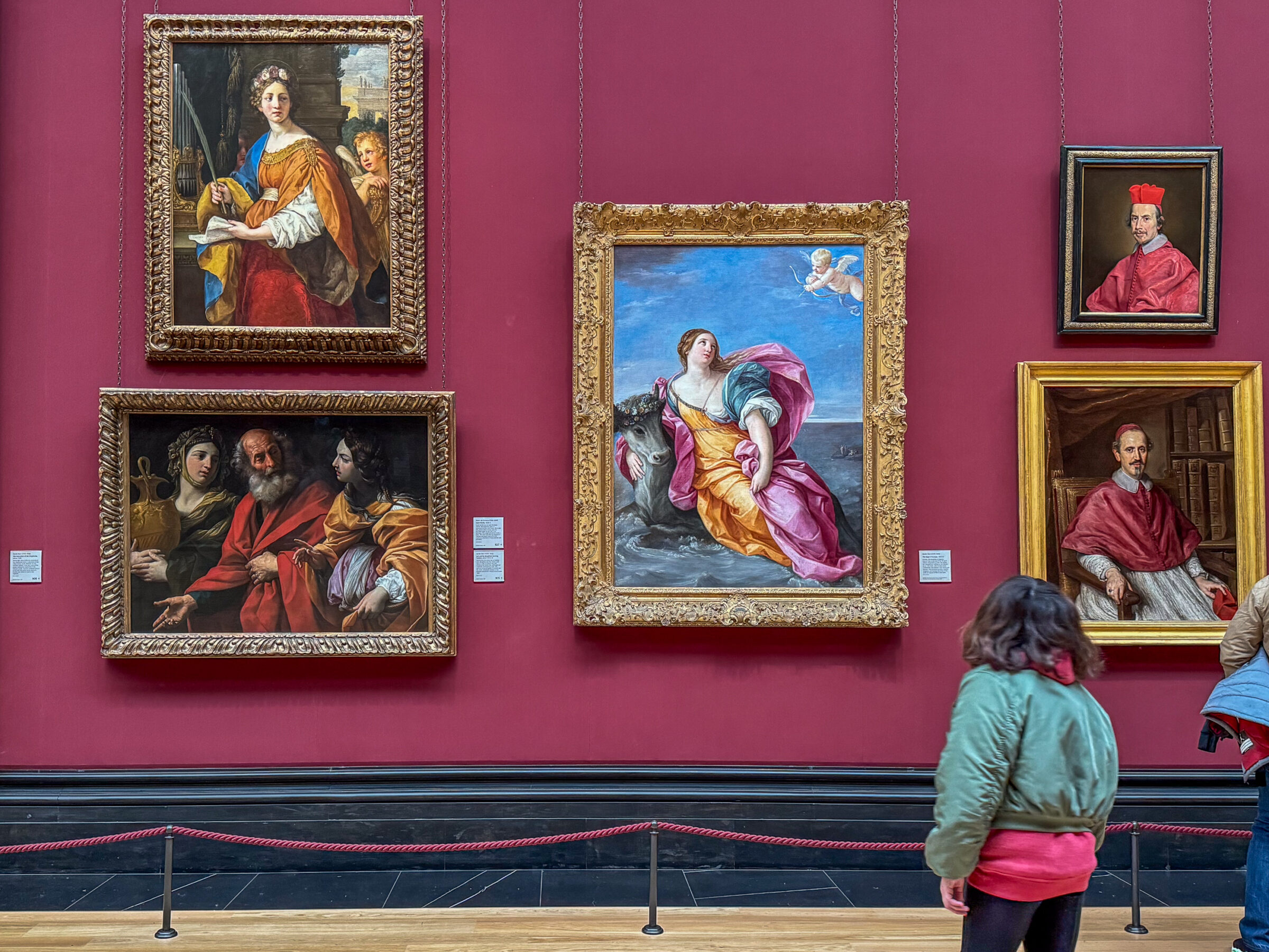 photo taken in an art gallery with a number of paintings on a red wall